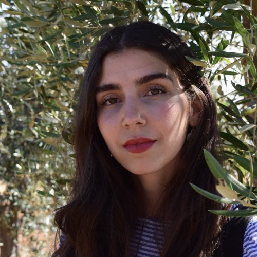 Headshot of woman in front of tree, looking directly at camera. 